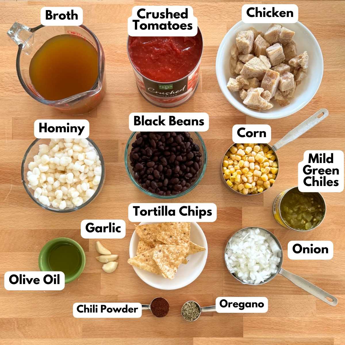 Labeled ingredients to make chicken tortilla soup: chicken,  black beans, corn, hominy, crushed tomatoes, diced onion, broth, tortilla chips, mild green chiles, olive oil, garlic, chili powder, and oregano.