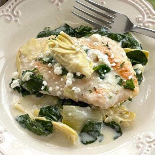 Serving of spinach artichoke chicken with a lemon cream sauce on a plate.