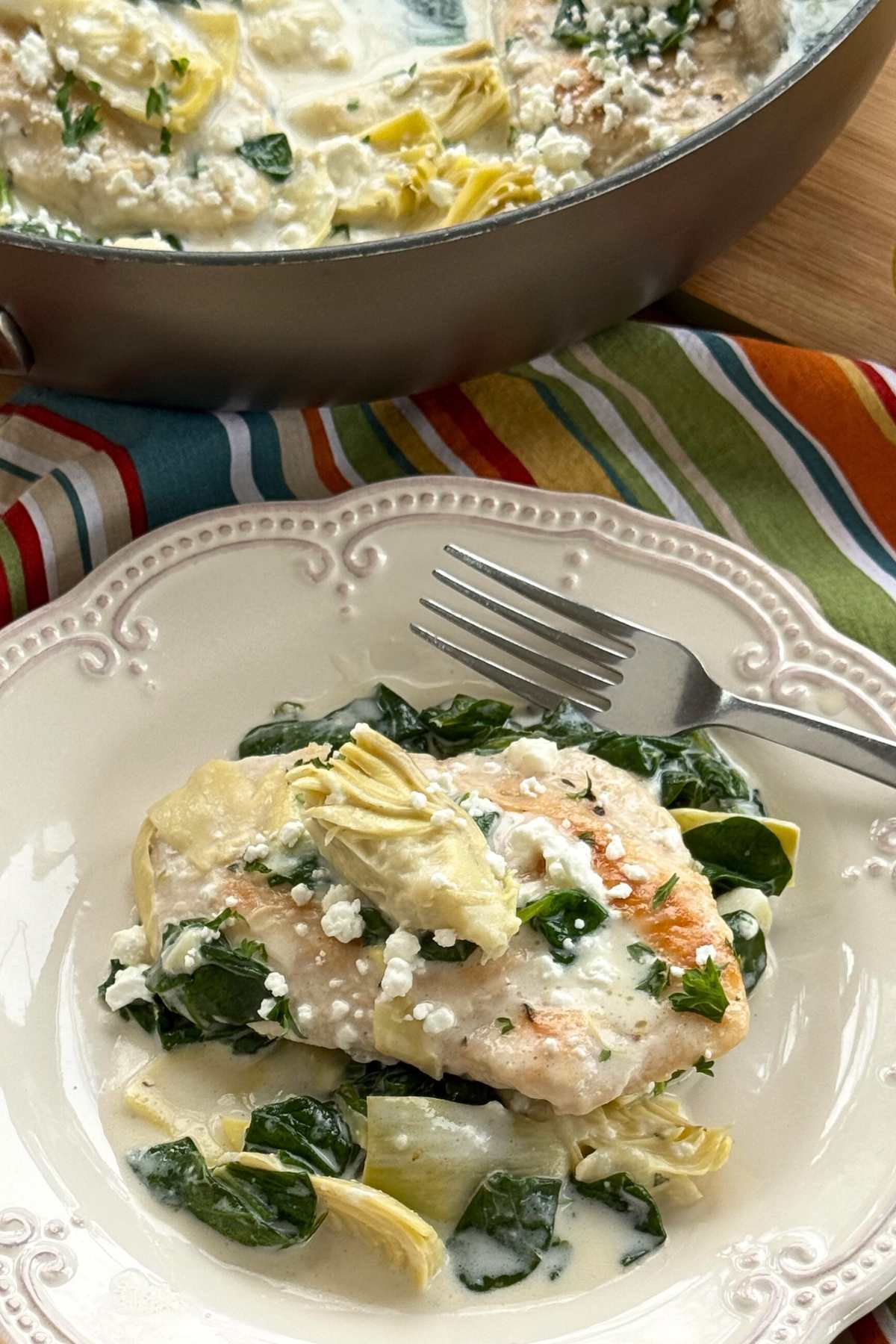 Serving of chicken with spinach and artichokes in a lemon cream sauce topped with goat cheese.