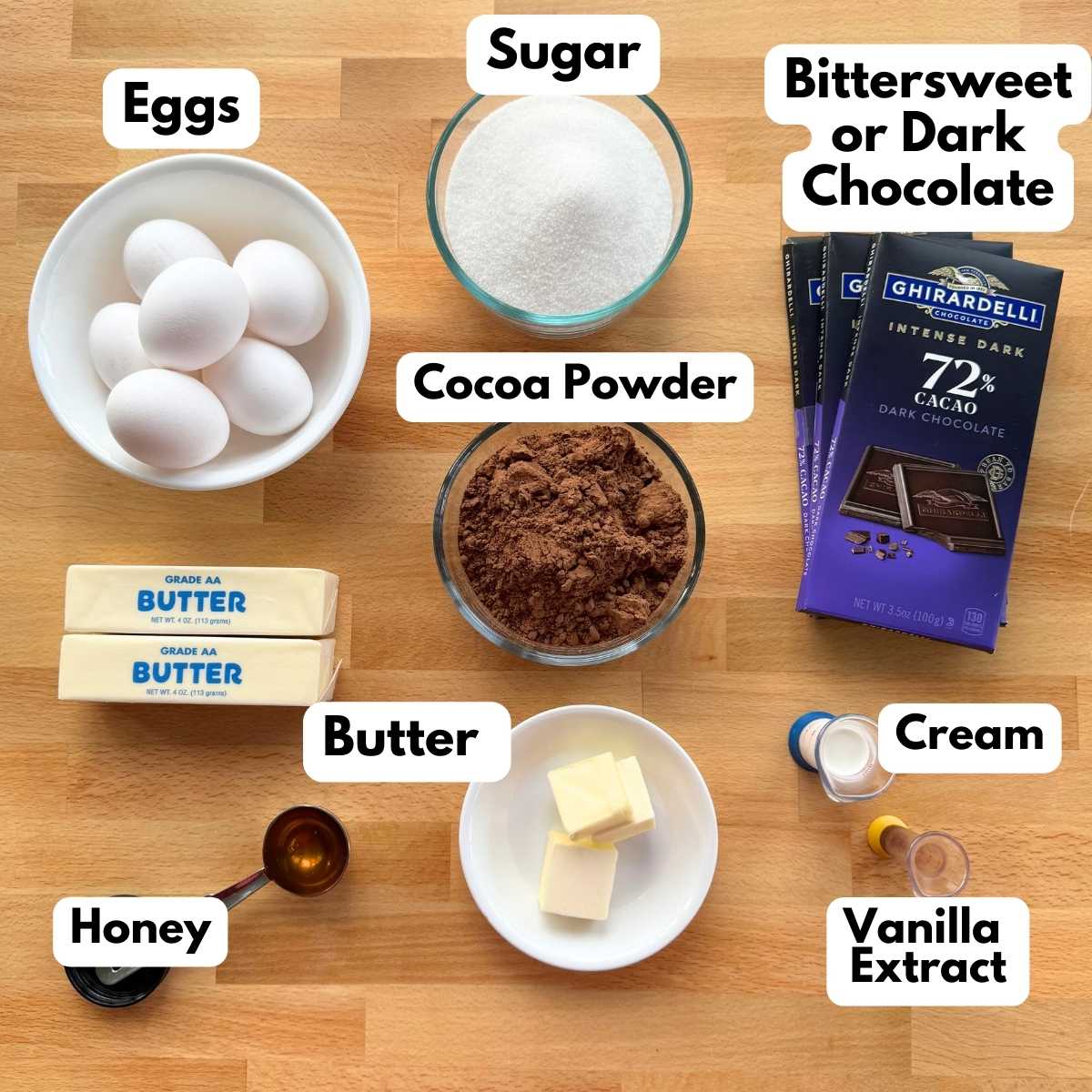 Ingredients to make cake and ganache recipe: chocolate bars, eggs, sugar, cocoa powder, butter, cream, honey, and vanilla extract.