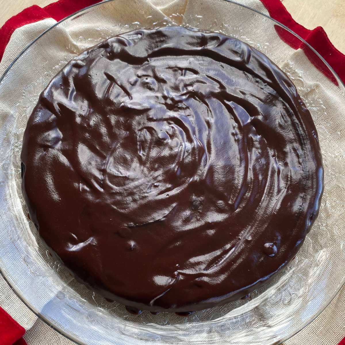 Full flourless chocolate cake with a silky chocolate ganache on a glass plate.