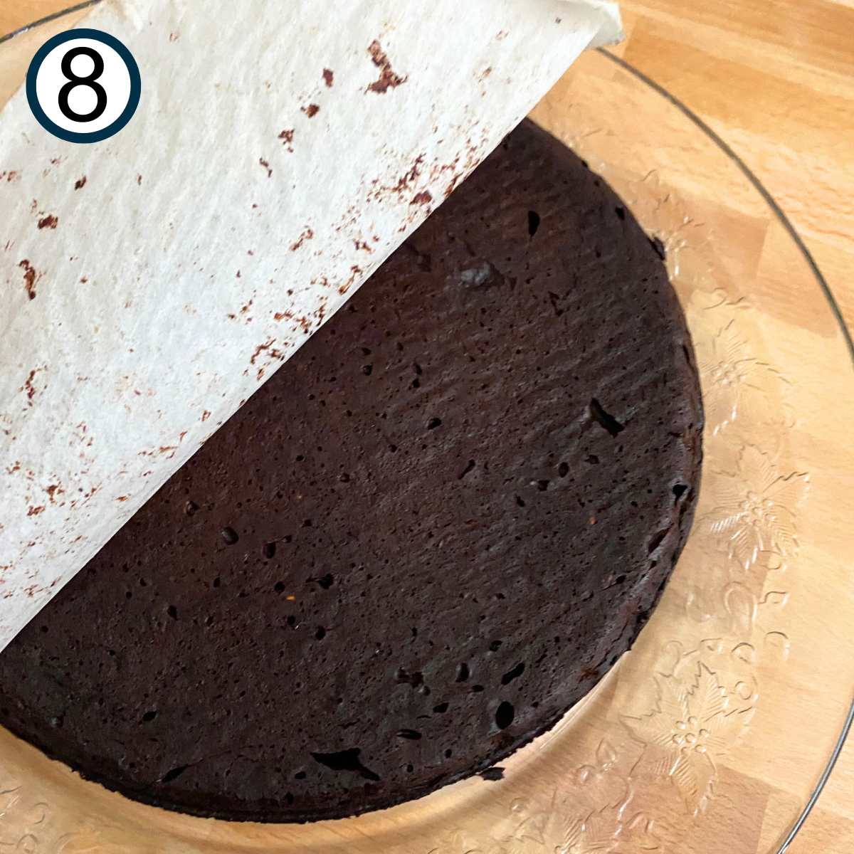 Inverted flourless chocolate cake with parchment paper being peeled off the top of the cake.