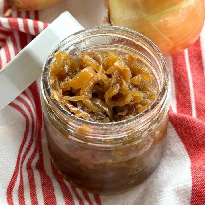 Slow cooker caramelized onions in a mason jar with onions in the background.