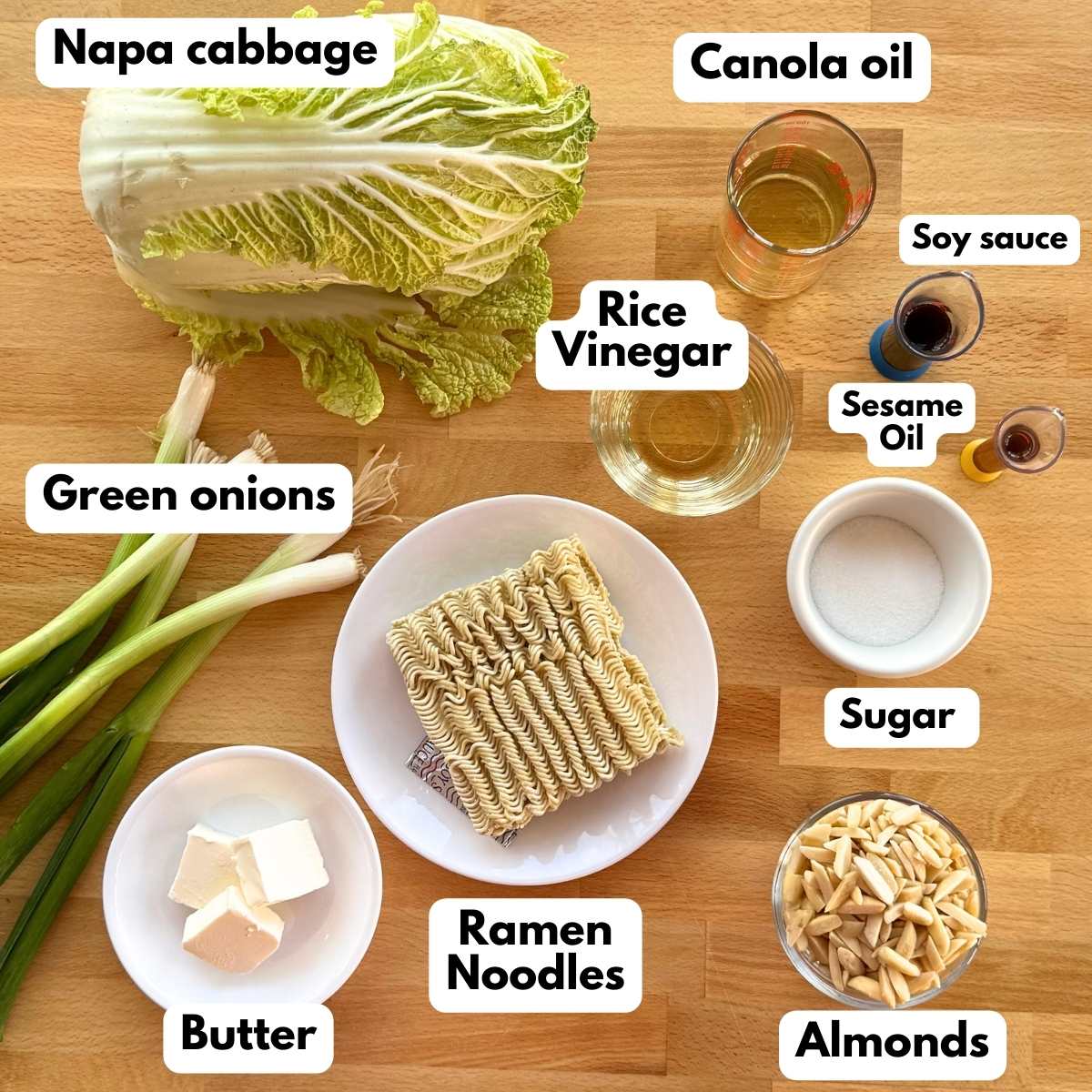 Labeled ingredients to make recipe: Napa cabbage, green onions, canola oil, rice vinegar, soy sauce, sesame oil, sugar, ramen noodles, butter, and slivered almonds.