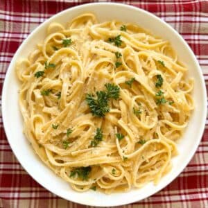 One pot fettuccine alfredo pasta on a white plate garnished with fresh parsley and sprinkled with Parmesan cheese.