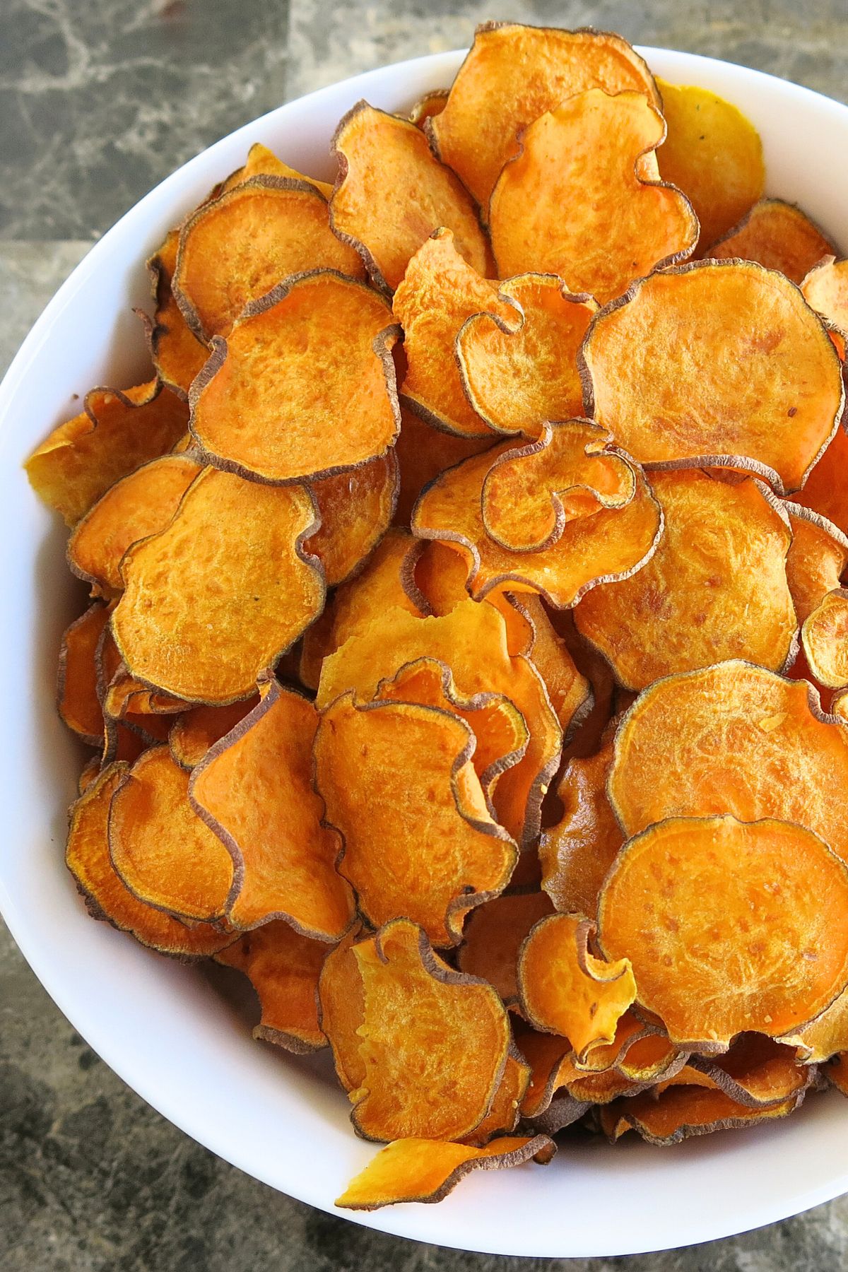 Large white bowl filled with oven-baked sweet potato chips on a marble background.