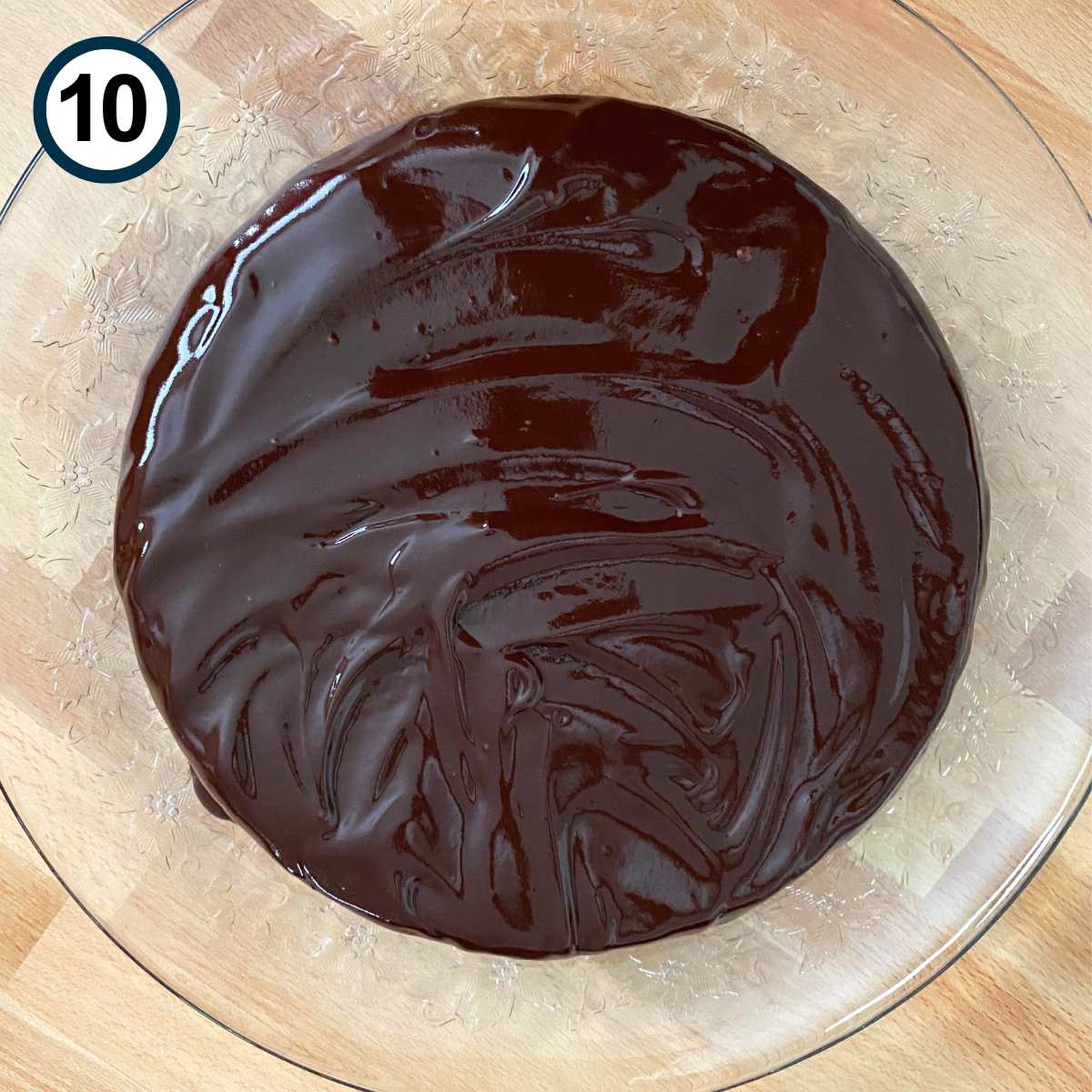 Chocolate ganache poured over flourless chocolate cake on a glass plate.