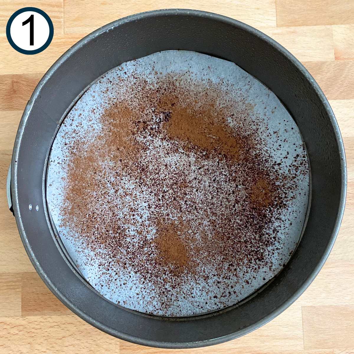 Springform pan with parchment paper in the bottom with a touch of cocoa powder on top.