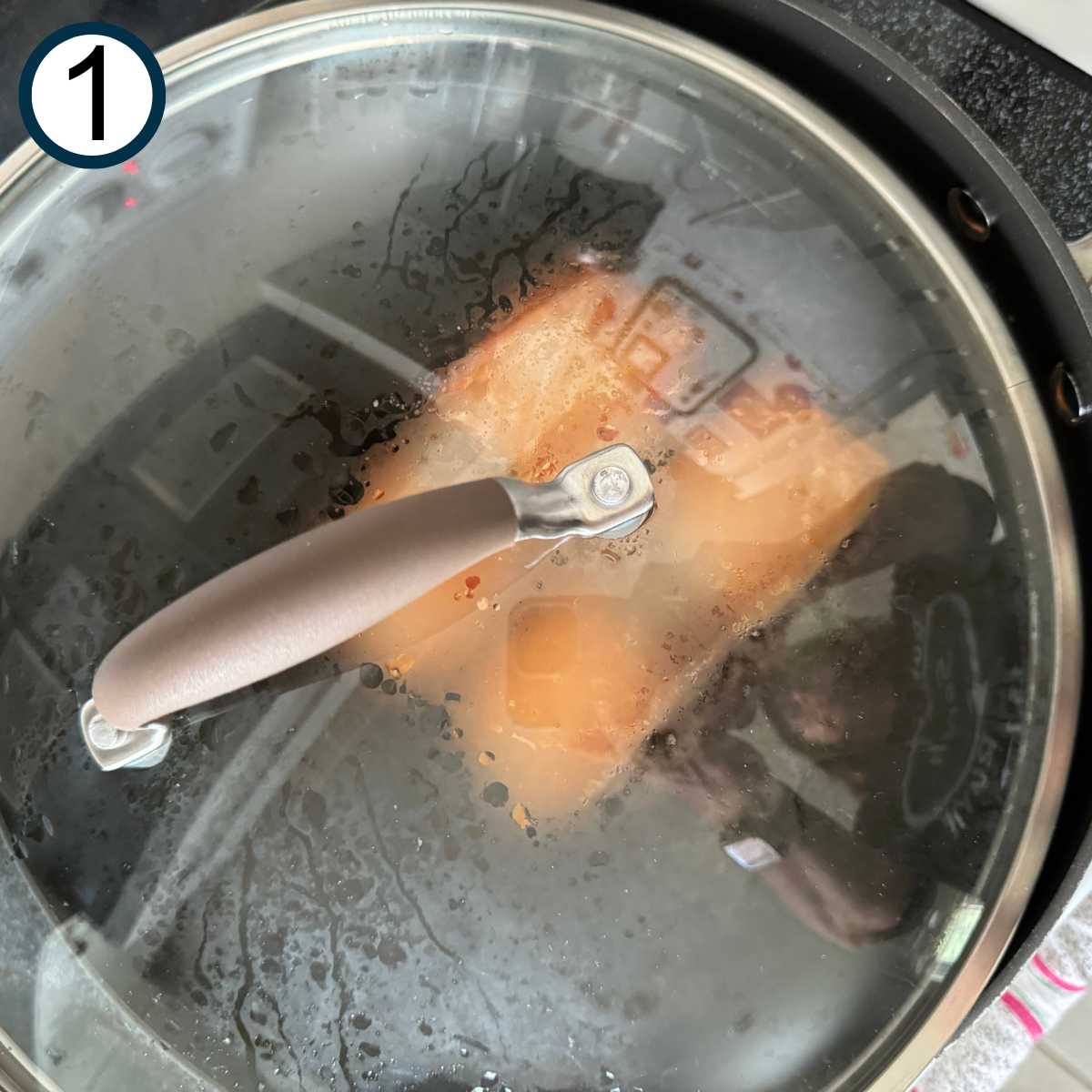 Salmon fillets in a large non-stick skillet, partially covered with a lid.