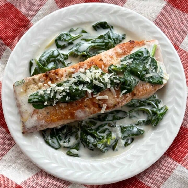 A serving of salmon florentine with a creamy spinach sauce on a white plate.