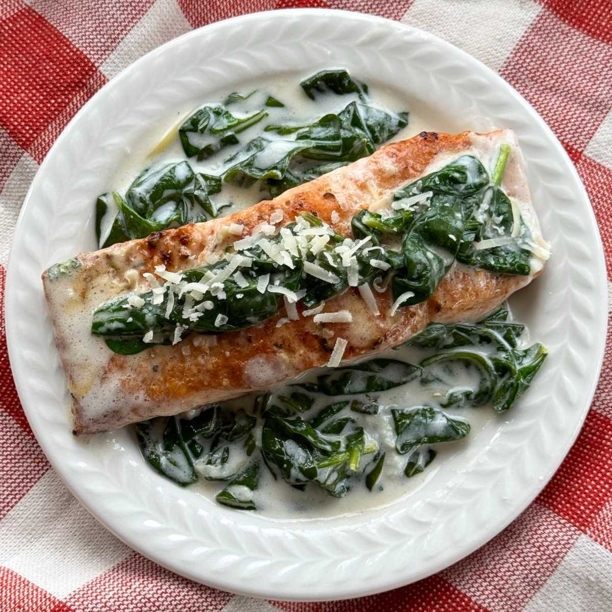 A serving of salmon florentine with a creamy spinach sauce on a  white plate.