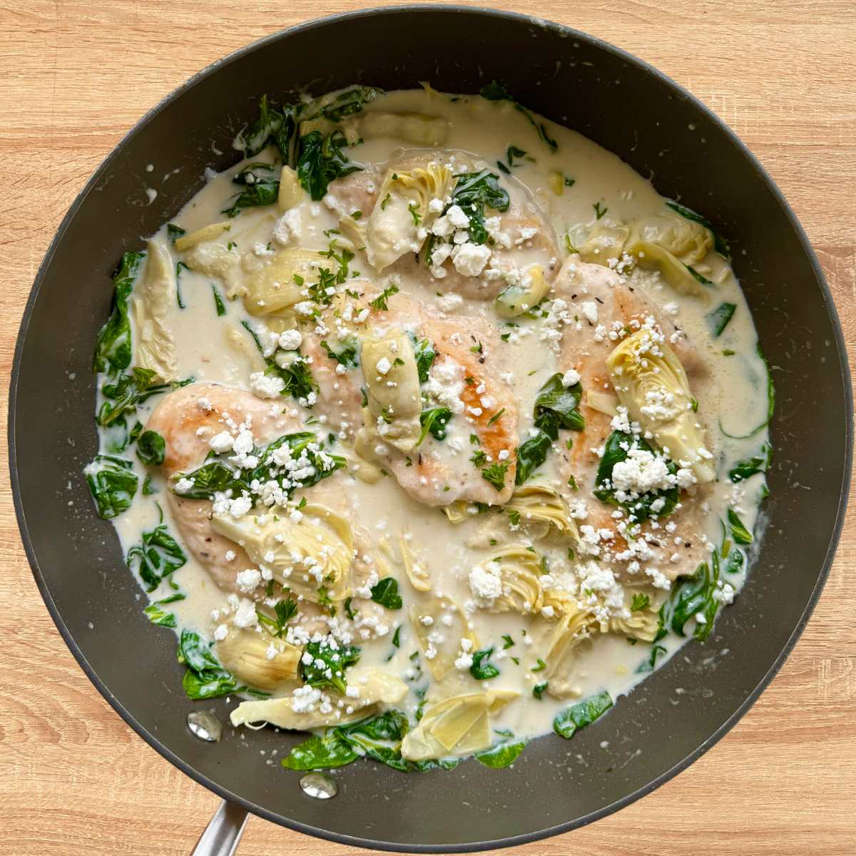 Spinach artichoke chicken in a skillet covered in a creamy lemon sauce and topped with goat cheese.