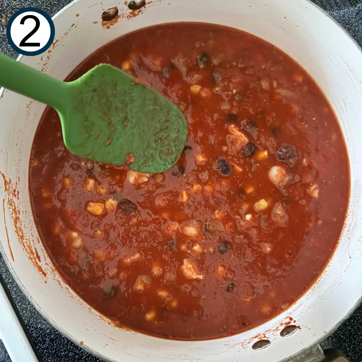 Green spatula stirring chicken tortilla soup ingredients in a pot.