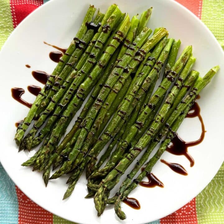 Roasted asparagus drizzled with balsamic glaze on a white plate.