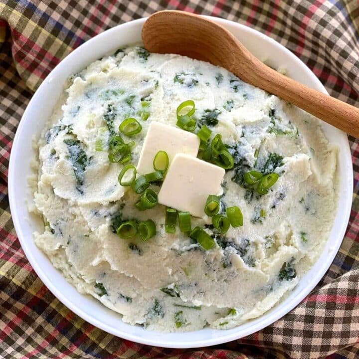 Creamy cauliflower colcannon topped with butter and green onions in a white bowl with a spoon.