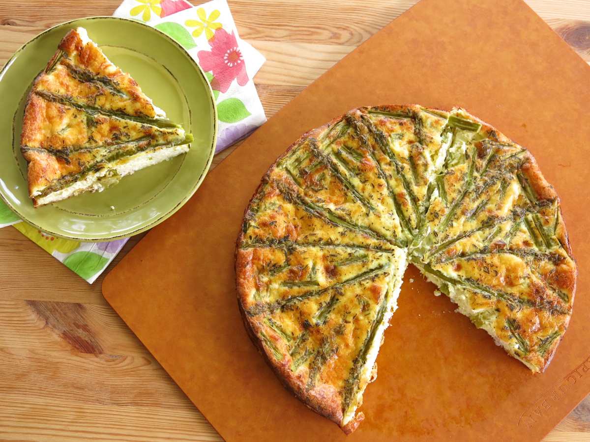 Crustless asparagus quiche on a cutting board with a slice removed and on a green plate next to it.