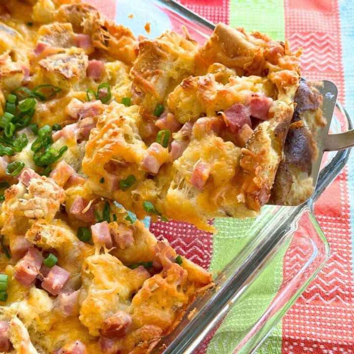 Spatula lifting a serving of ham strata out of the corner of a glass baking dish.