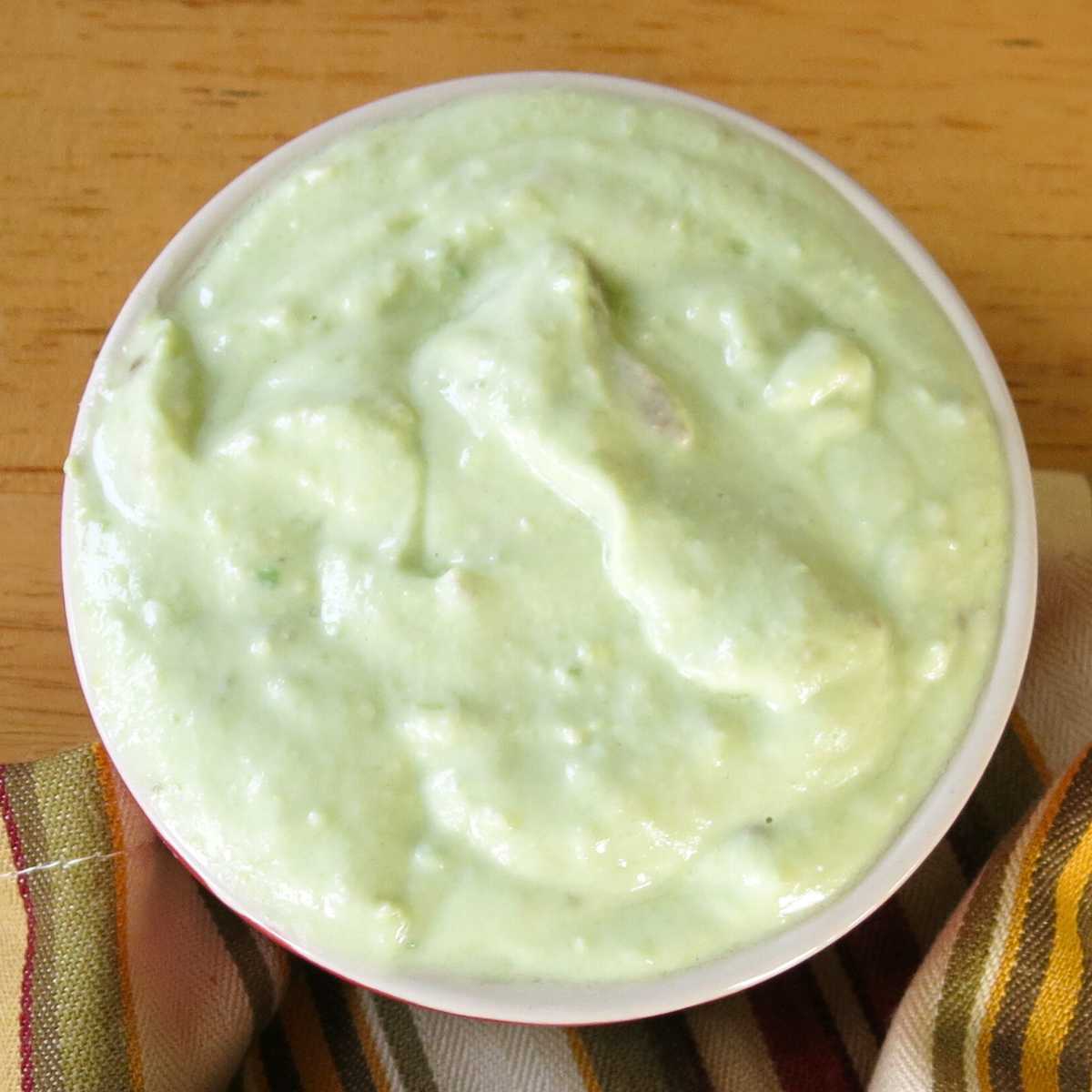 Avocado cream sauce made with Greek yogurt in a red bowl.