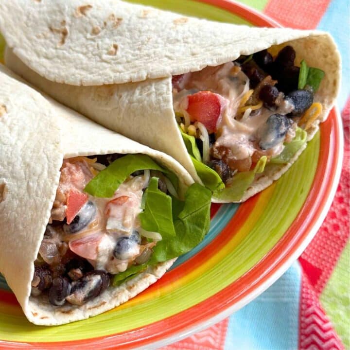 Two vegetarian black bean wraps with lettuce, cheese and salsa yogurt sauce on a colorful plate.