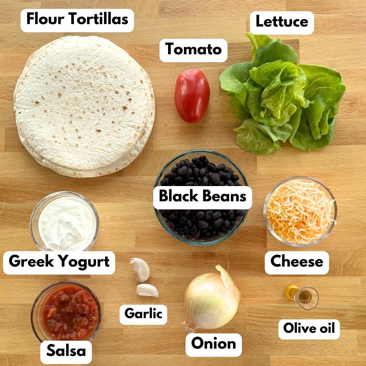 Ingredients to make recipe: stack of flour tortillas, bowl of black beans, bowls of Greek yogurt, salsa, and cheese, onion, two garlic cloves, lettuce leaves, Roma tomato, onion, and measuring container with olive oil.