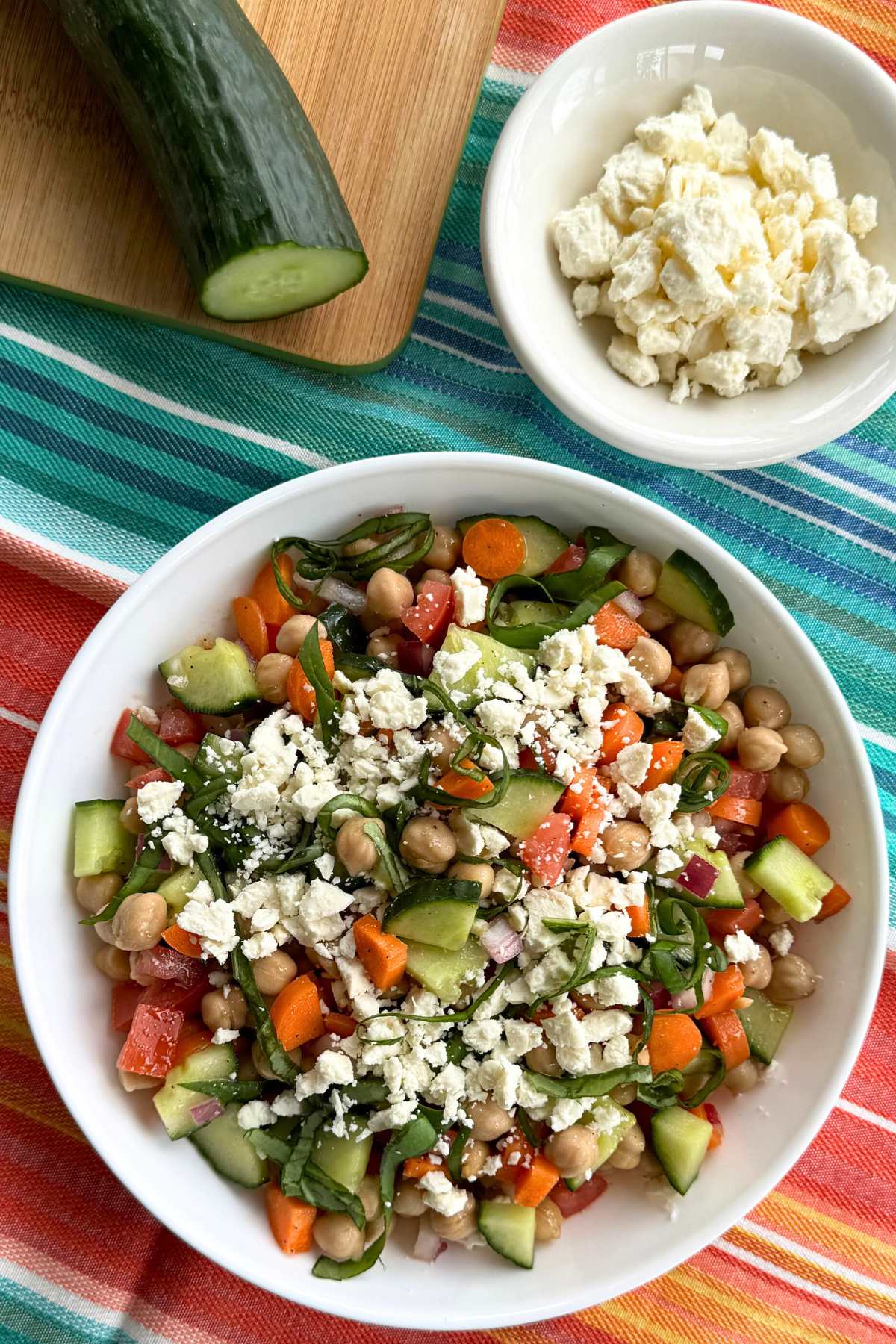 Chickpea Salad in a shallow white bowl with a bowl of feta cheese and an English cucumber behind it.