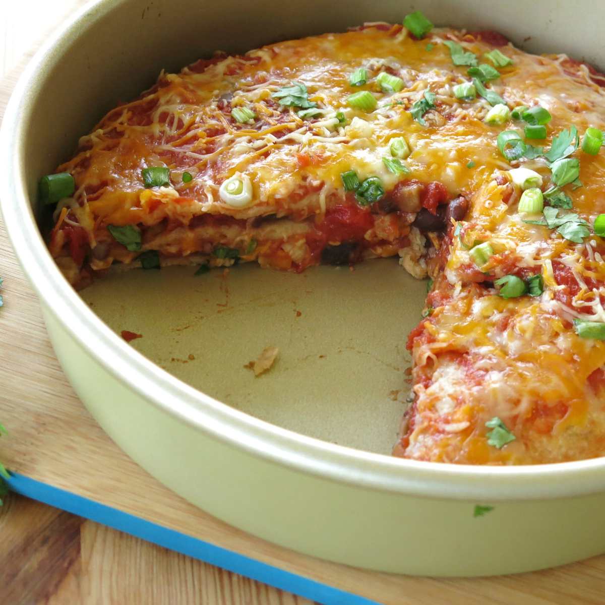 Layered burrito pie casserole in a round tin with a slice missing, exposing the layers.