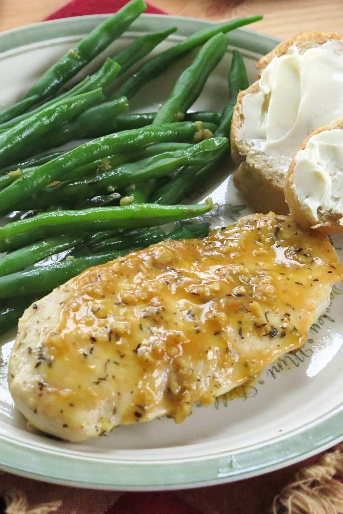 One lemon chicken cutlet drizzled with lemon garlic sauce on a plate with green beans and buttered bread.