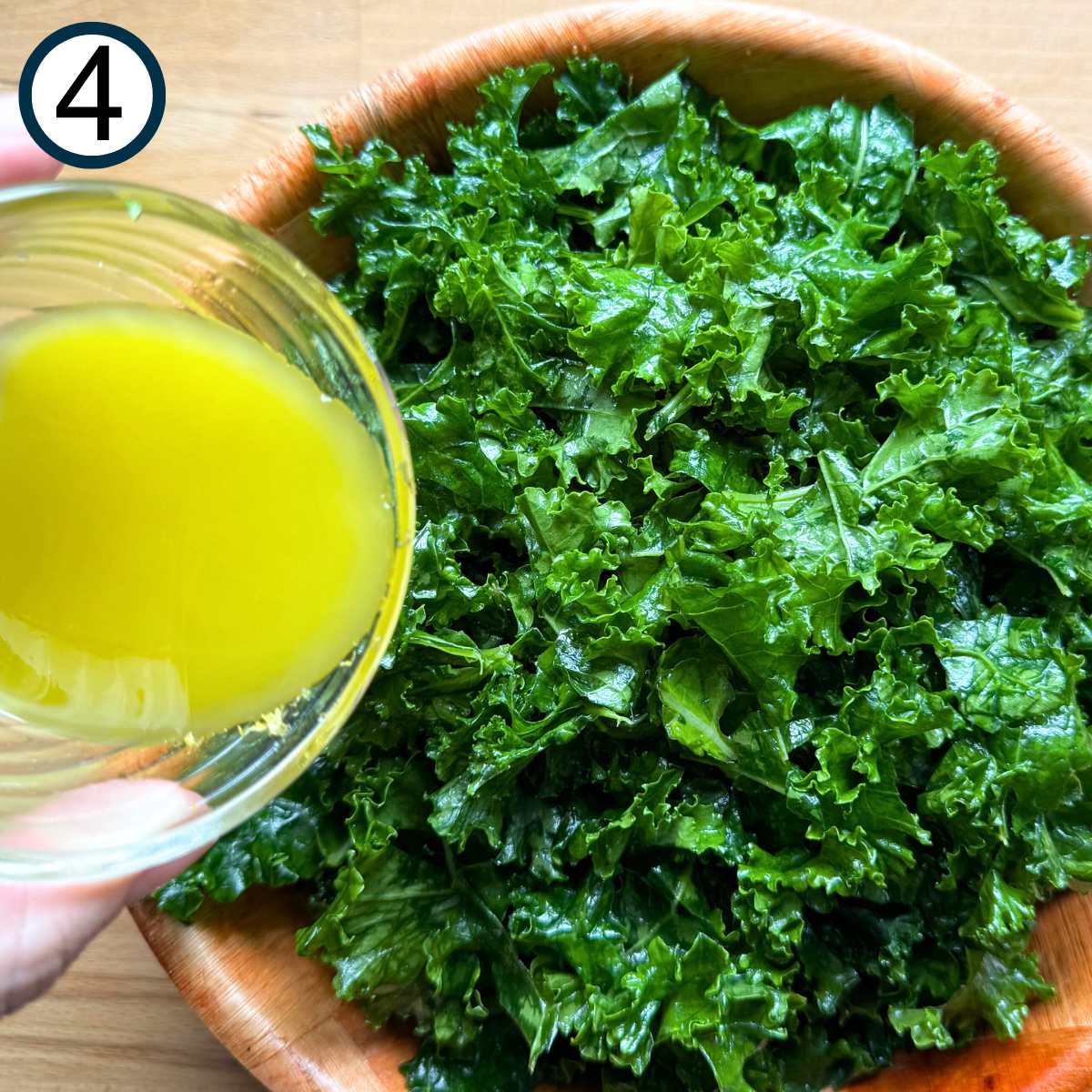 Lemon dressing being poured over massaged kale leaves.