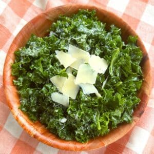 Massaged kale salad topped with shaved Parmesan and lemon dressing in a brown bowl on a orange checkered background.