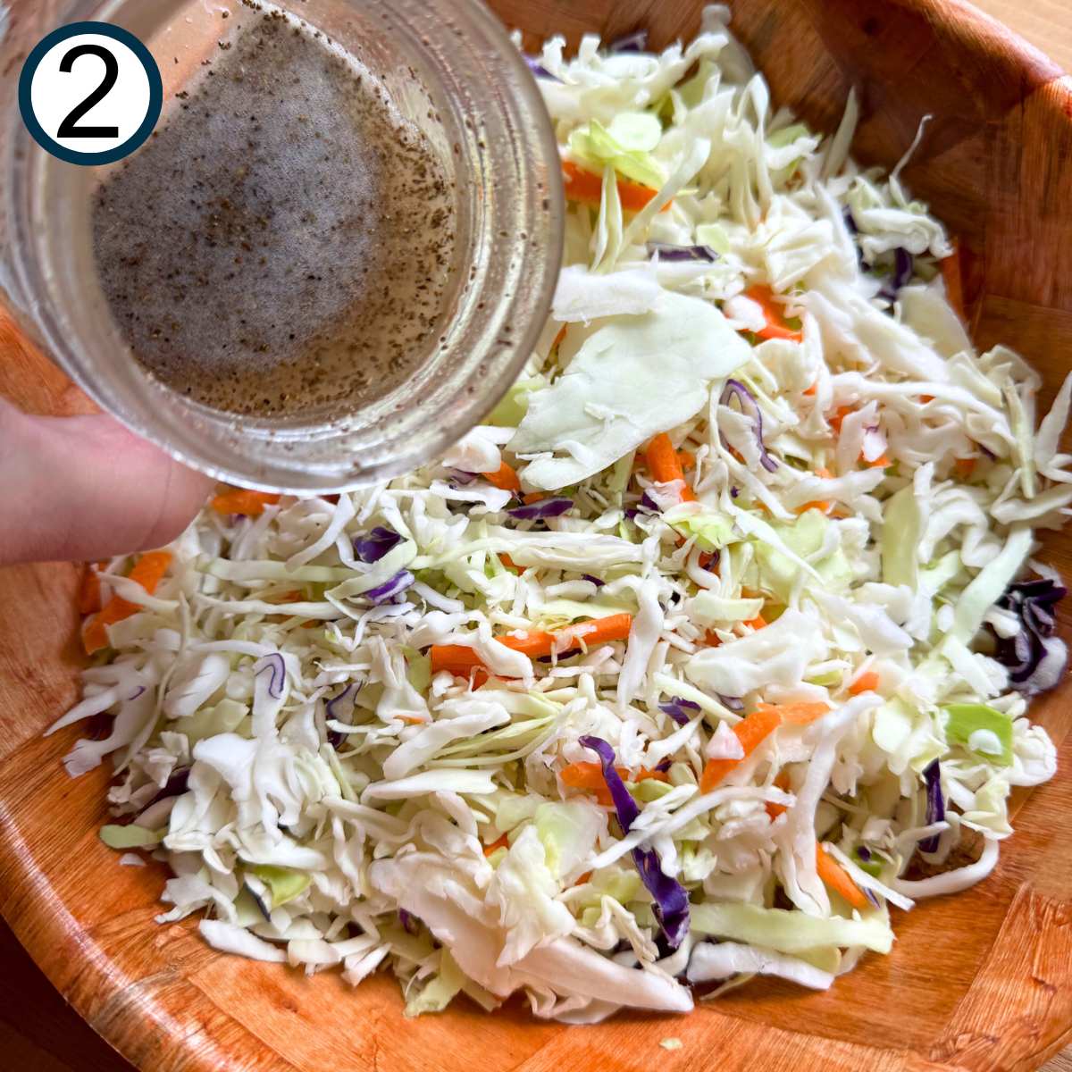 Vinegar dressing being poured over shredded cabbage and carrots.