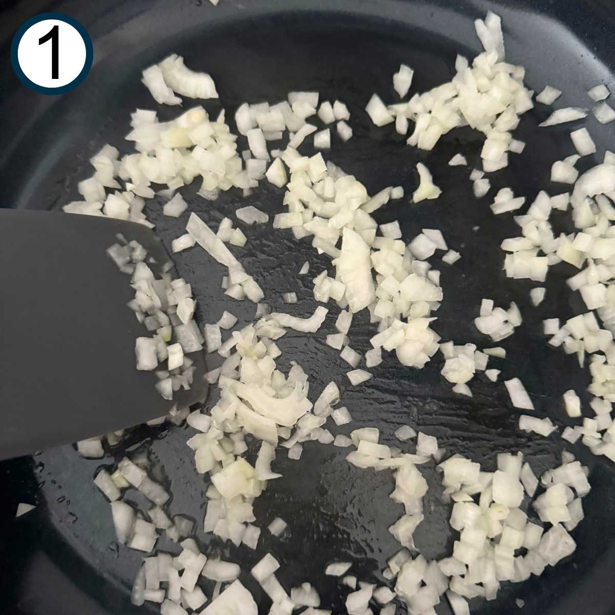 Diced onion and garlic in a large skillet being sauteed with a spatula.