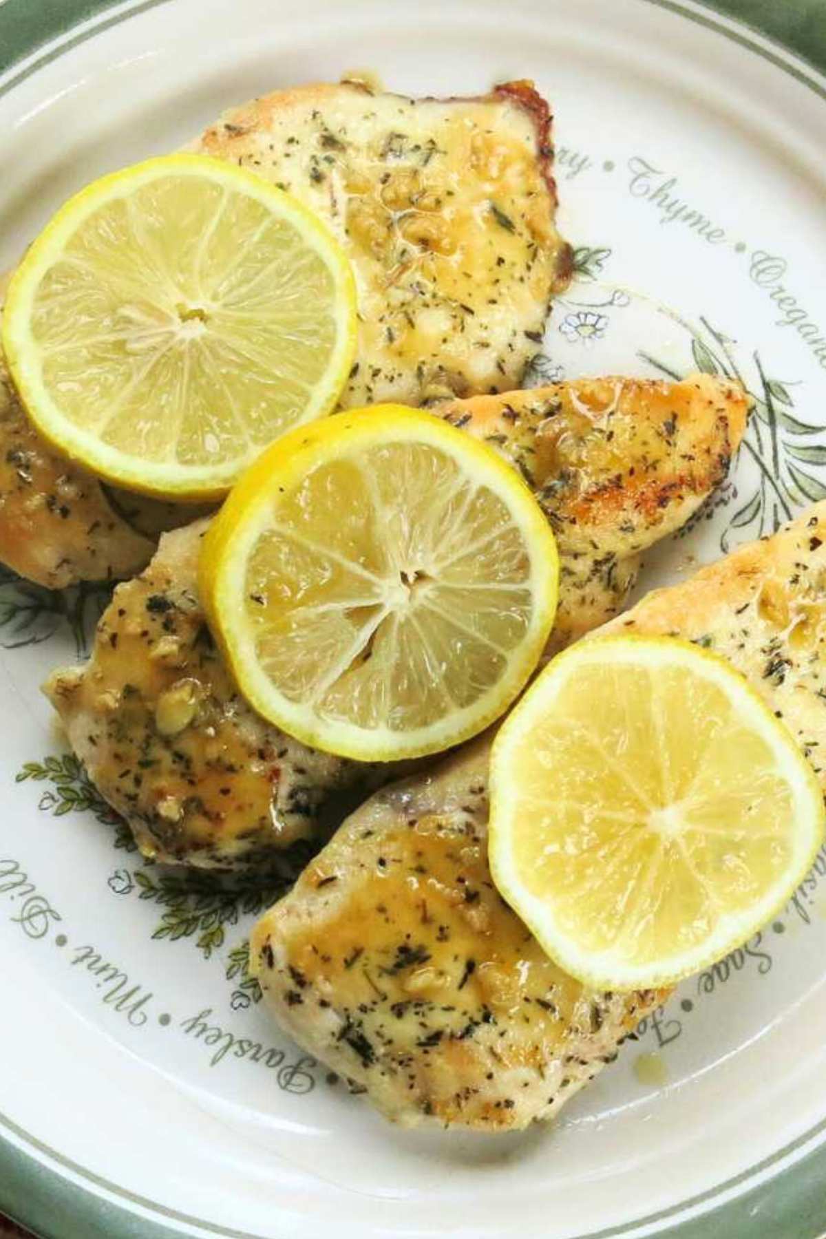 Three lemon chicken cutlets on a plate drizzled with a lemon garlic sauce and topped with three lemon slices.