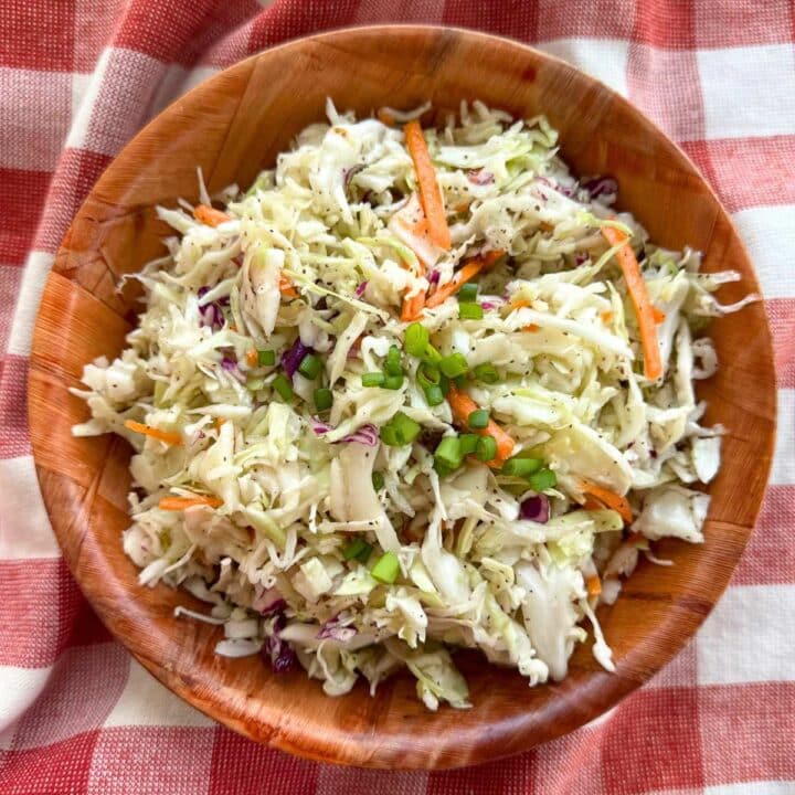 Southern coleslaw with vinegar dressing in a brown bowl on top of a red checkered cloth.