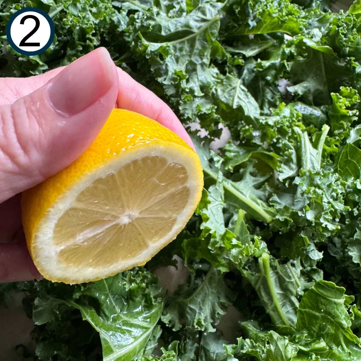 Hand holding half of a lemon over kale leaves.