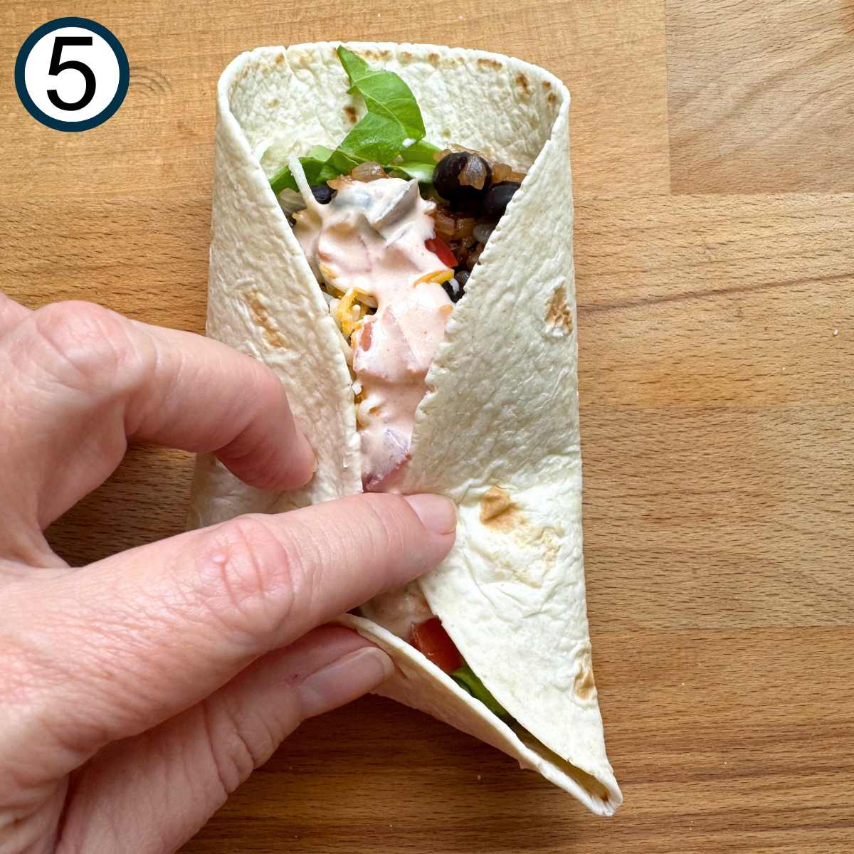 Hand rolling the bottom of the flour tortilla topped with the filling up and pulling the sides together.