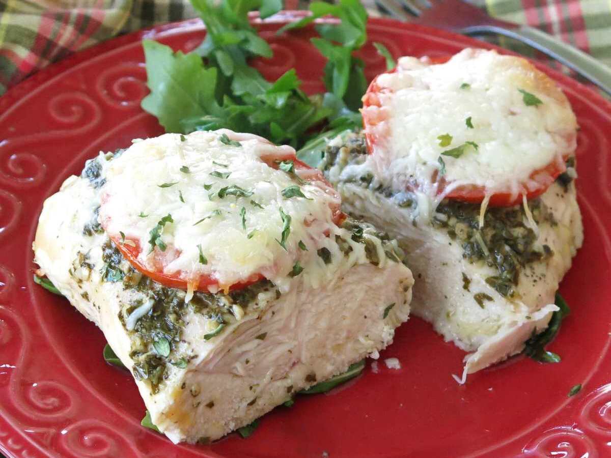 Baked pesto chicken with tomatoes mozzarella cut in half on a red plate.
