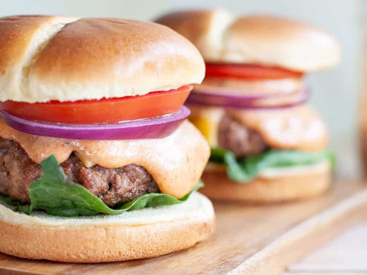 Two burgers with lettuce, tomato, and red onion, with burger sauce dripping voer the beef patty.
