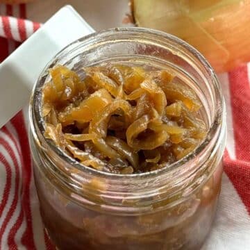 Caramelized onions in a glass mason jar with white lid resting against the side of the jar.