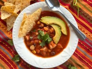 Chicken tortilla soup in a white bowl with a spoon topped with avocado slices and tortilla chips.