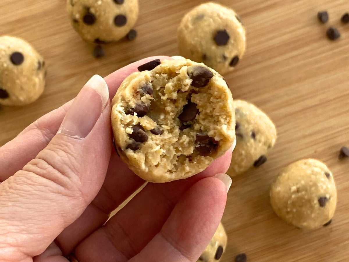 Fingers holding a chickpea cookie dough ball with a bite taken out with more cookie dough balls below it.