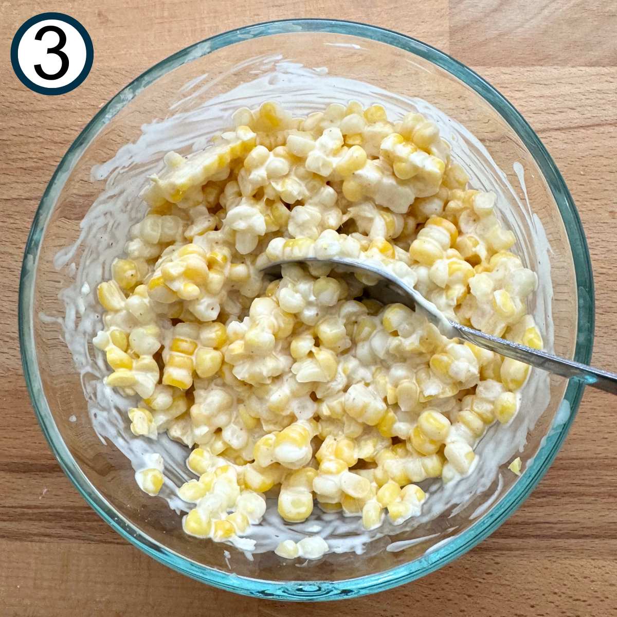 Corn kernels mixed with lime crema mixture in a glass bowl.