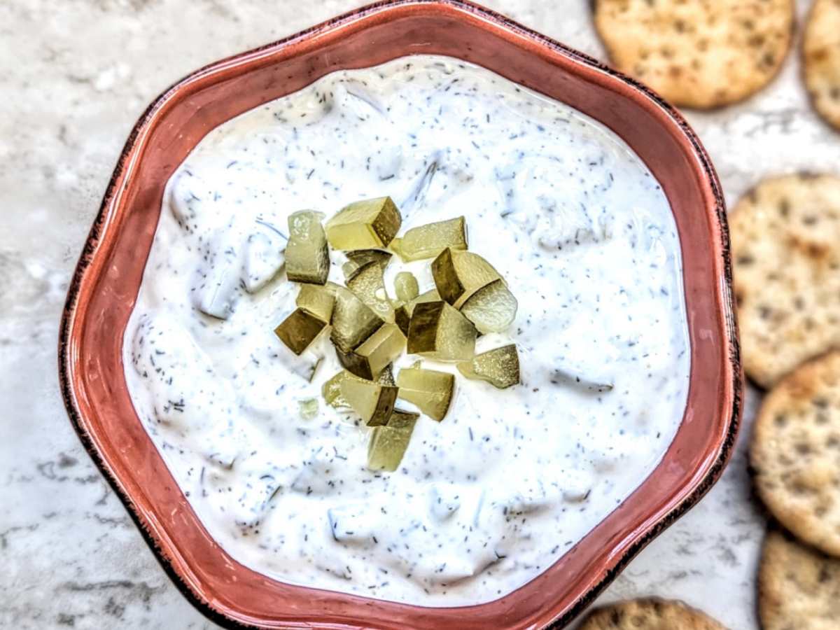 Dill pickle dip in a brown bowl with chopped pickles on top.