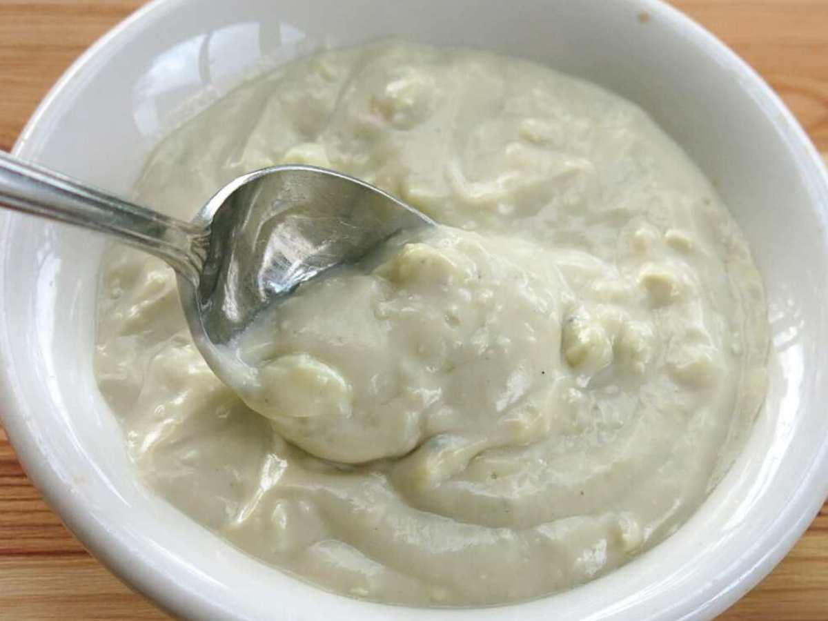 Spoon lifting blue cheese sauce out of a white bowl.