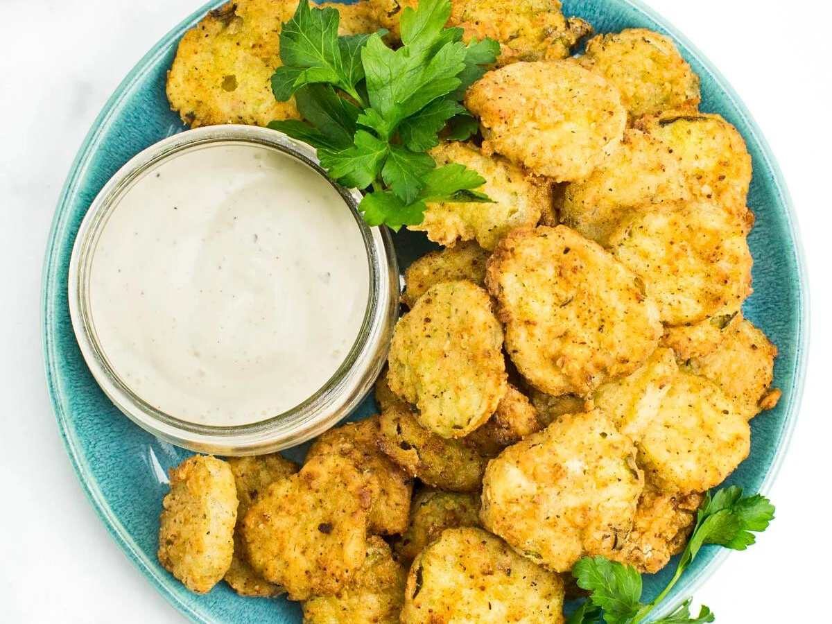 Fried pickles on a green plate with sauce and parsley garnish.