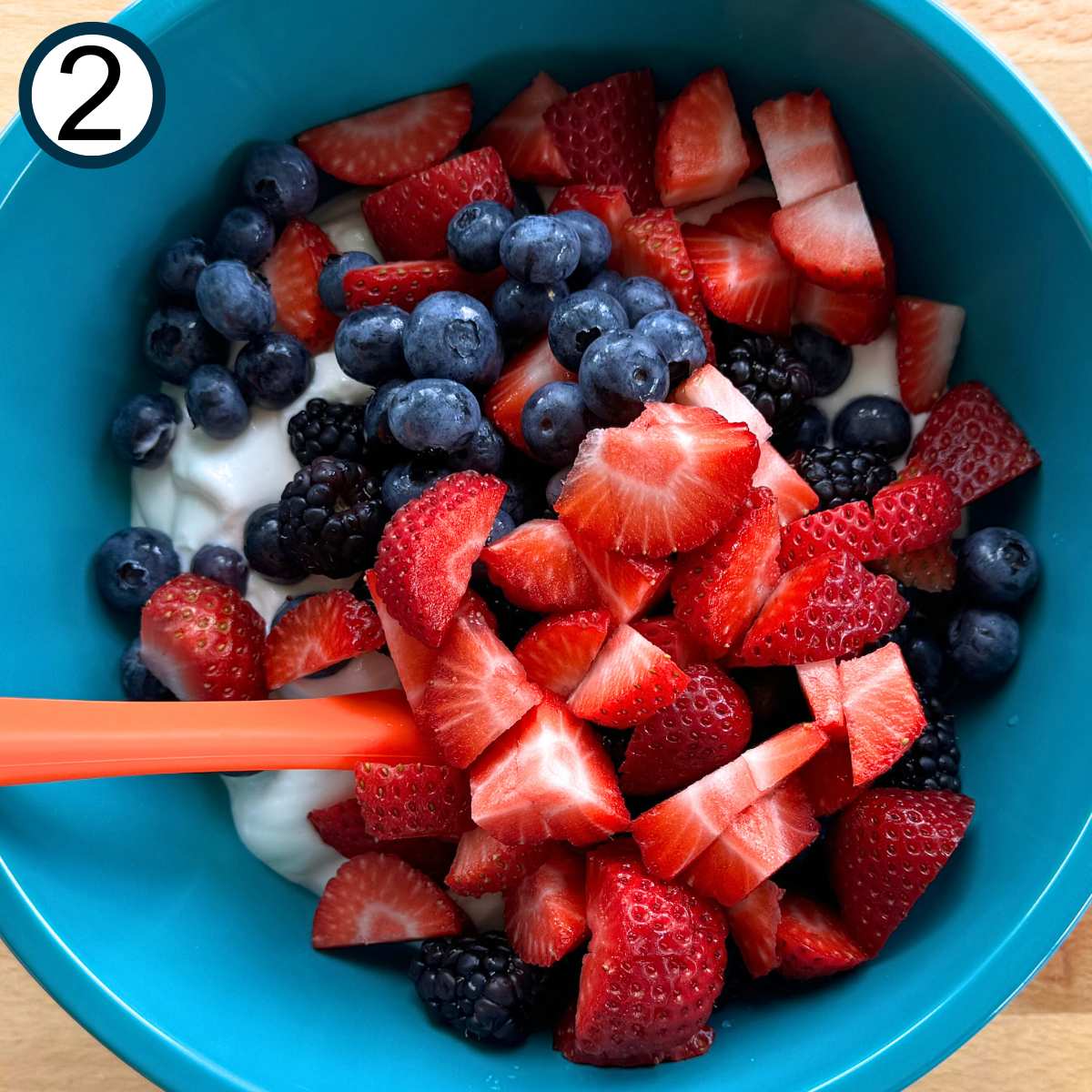 Blueberries, blackberries, and chopped strawberries on top of whipped cottage cheese in a turquoise bowl.