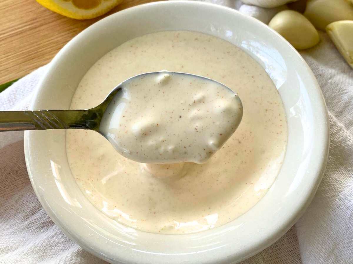 Spoon lifting lemon garlic aioli out of a white bowl.