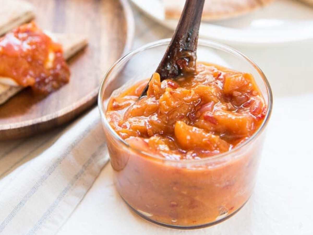 Peach chutney in a glass jar with a spoon.