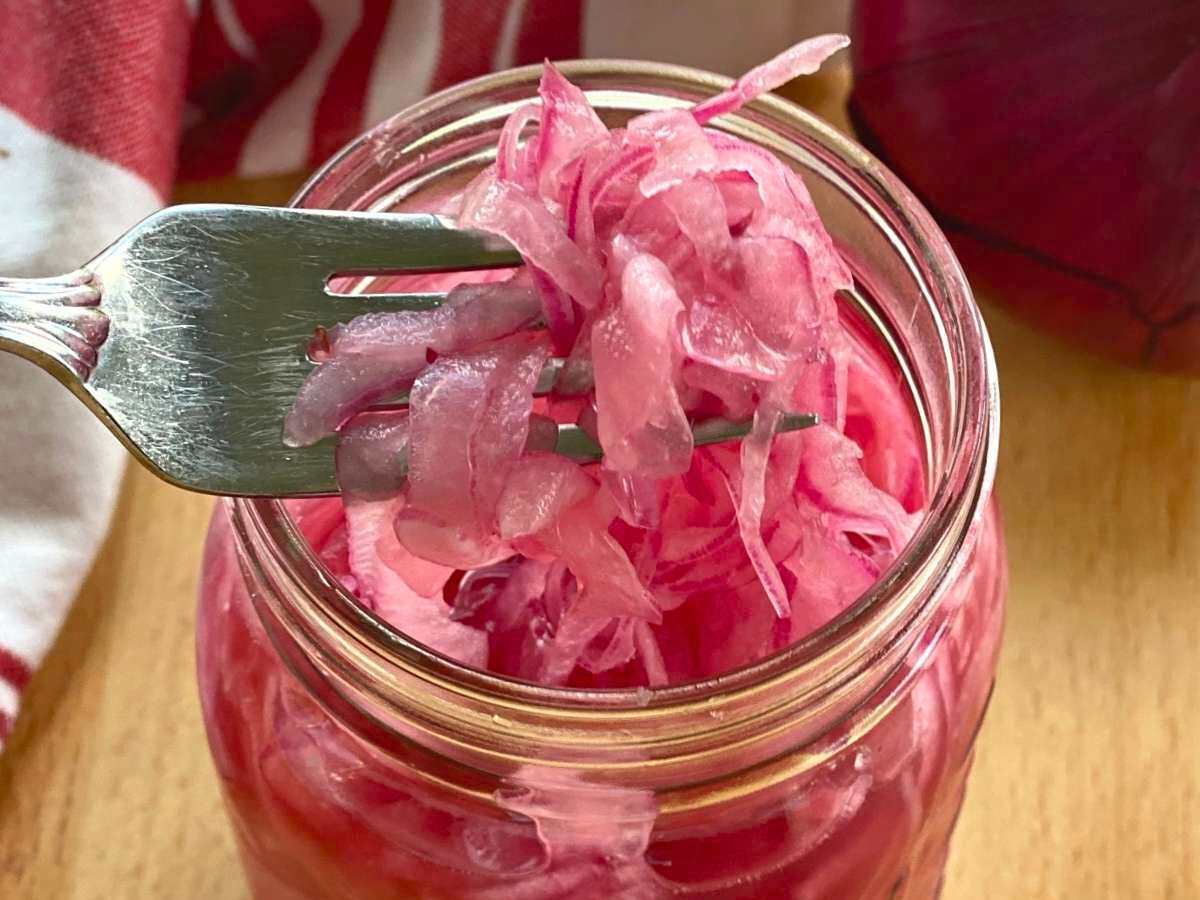 Fork lifting easy pickled red onions out of a mason jar.