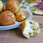 Plate of pizza cake pops with three cheese filling on a plate with one on the placemat with a bite removed exposing the gooey cheese.