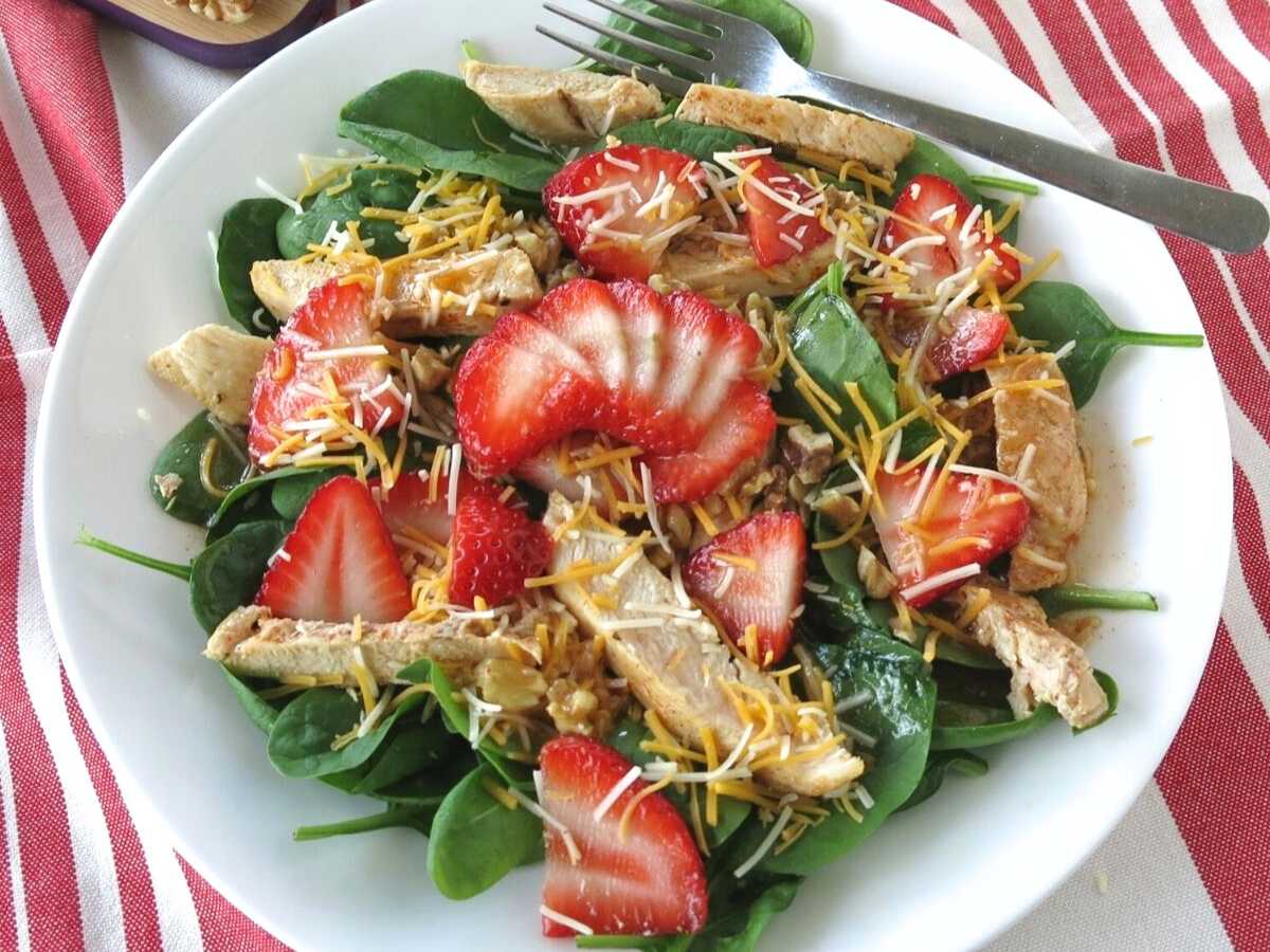 Strawberry spinach walnut salad in a white bowl with a fork.